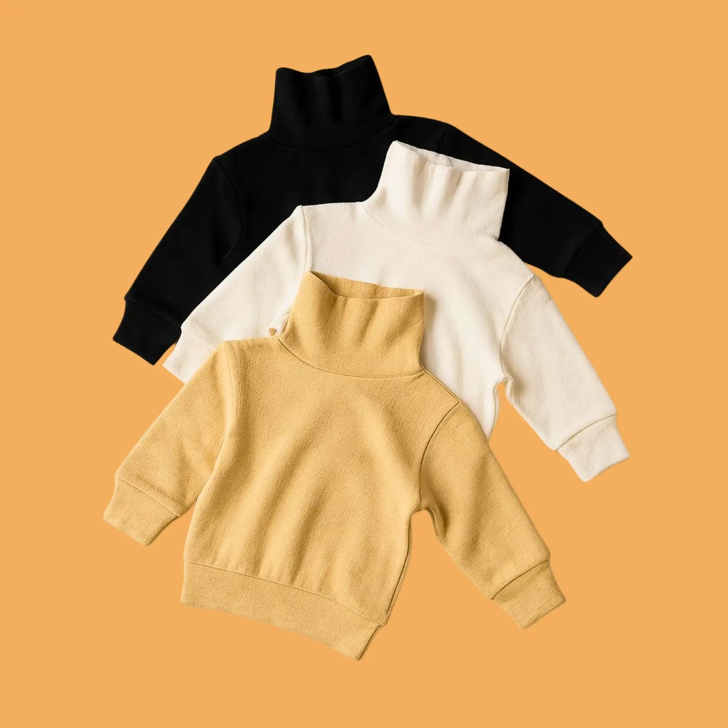 Three turtleneck sweaters in black, white, and beige on a mustard yellow background