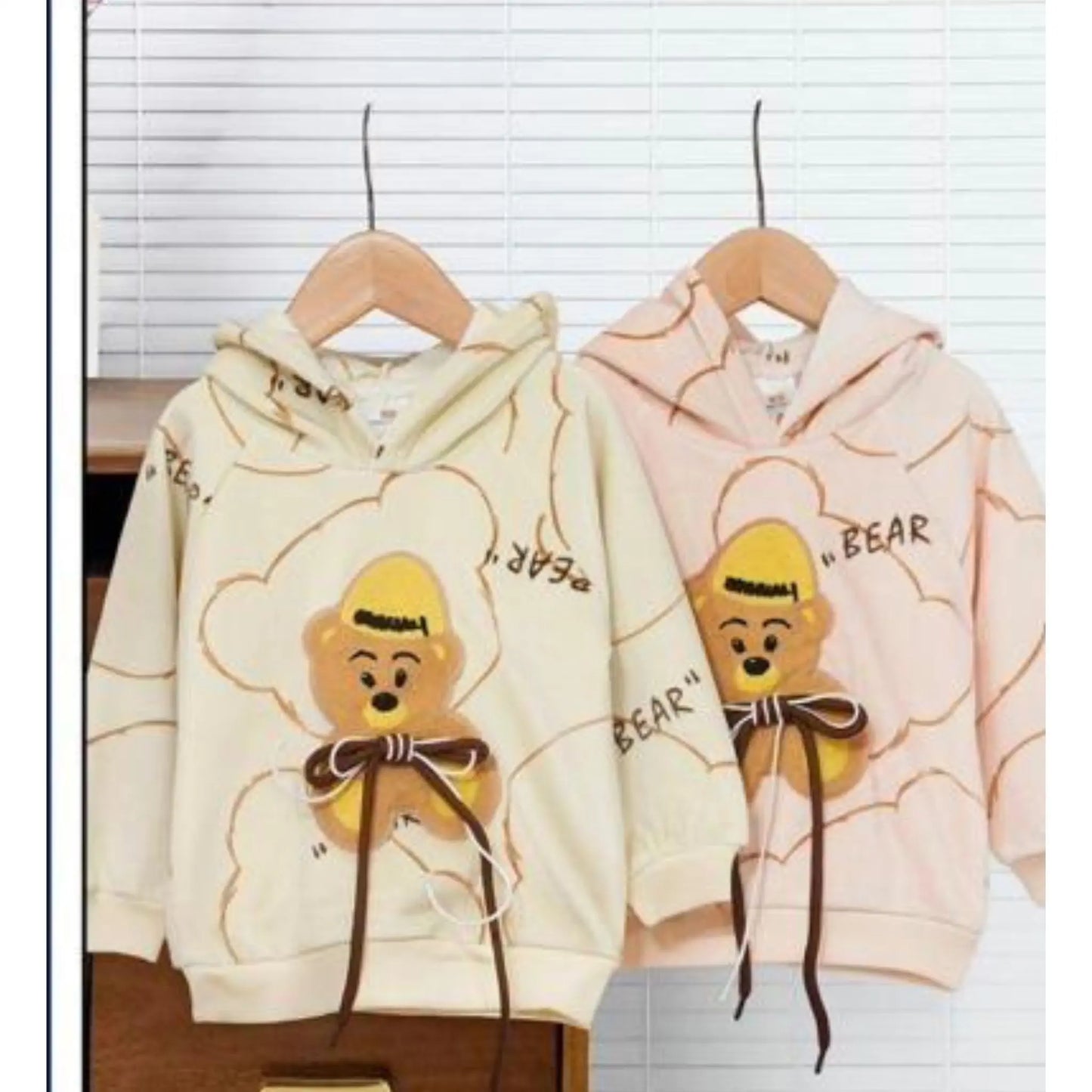 Two hoodies with cartoon bear designs on hangers against a white background.