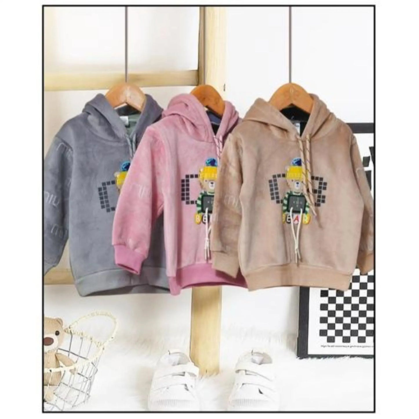 Three hoodies in gray, pink, and beige hanging on a rack with a checkered floor in the background.