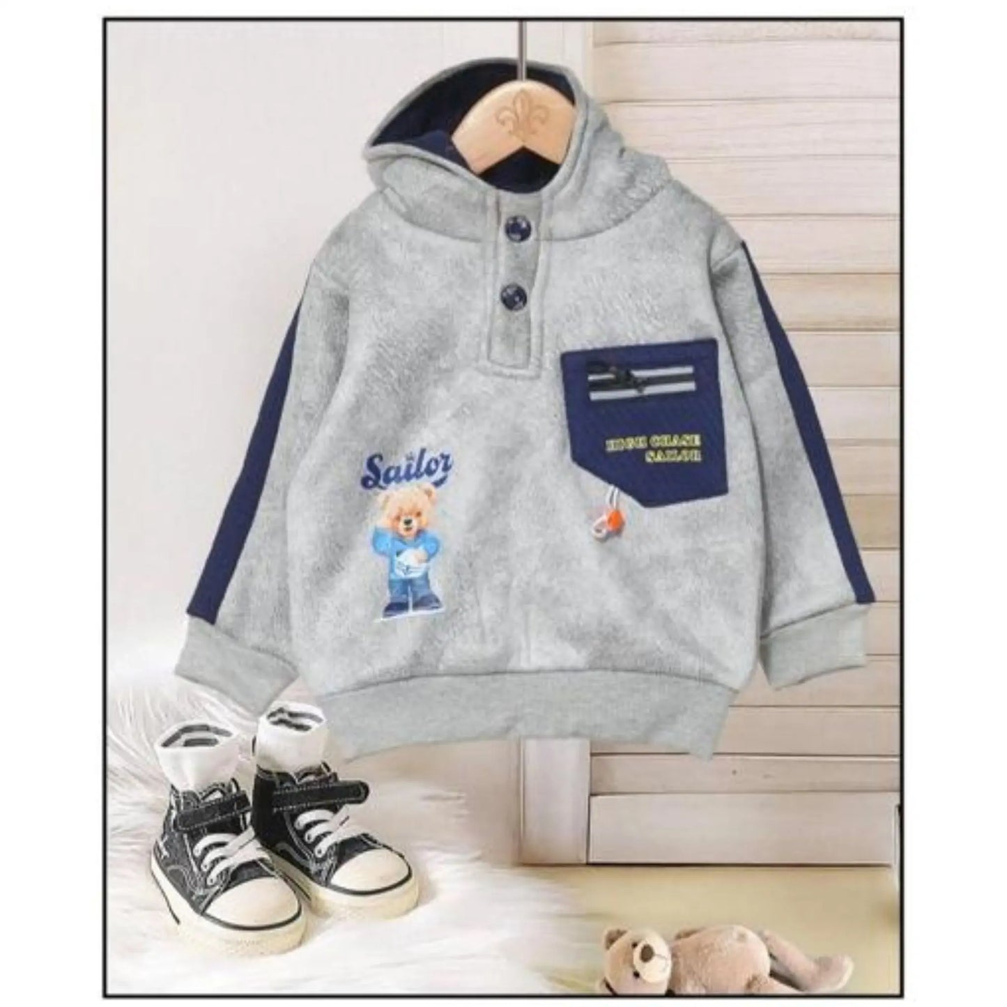 Gray hoodie with teddy bear design and text, paired with black sneakers on a light wooden floor.